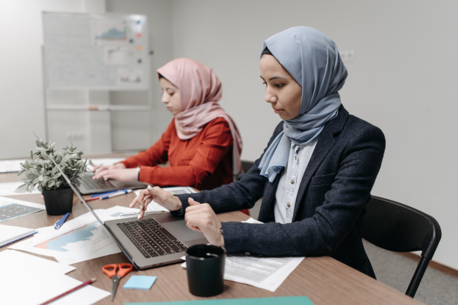 Two businesswomen working on laptops and reviewing financial reports in an office